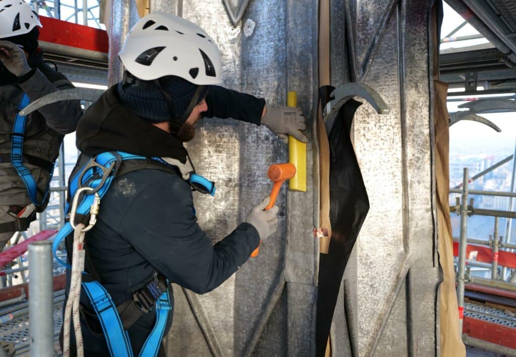 Roofer meticulously molding and shaping lead pieces for the roof of Notre-Dame Cathedral's spire.